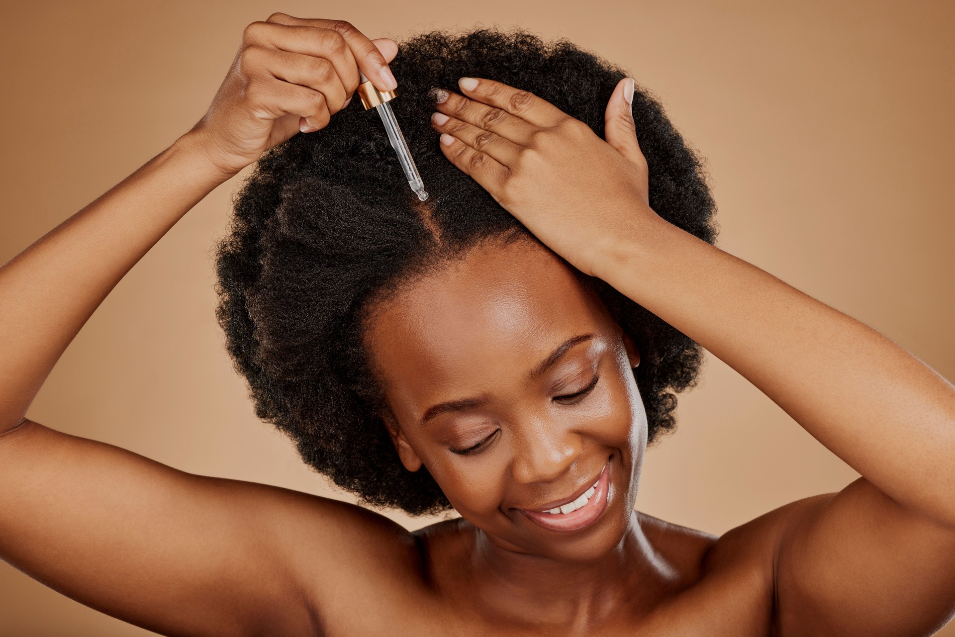 Oil serum, hair care or black woman with afro in studio on brown background for a healthy scalp. Smile, pipette or natural African girl at hairdresser salon for hairstyle treatment or beauty makeover